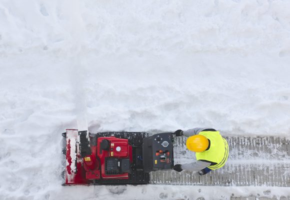 Worker cleaning snow on the sidewalk with a snowblower. Maintenance